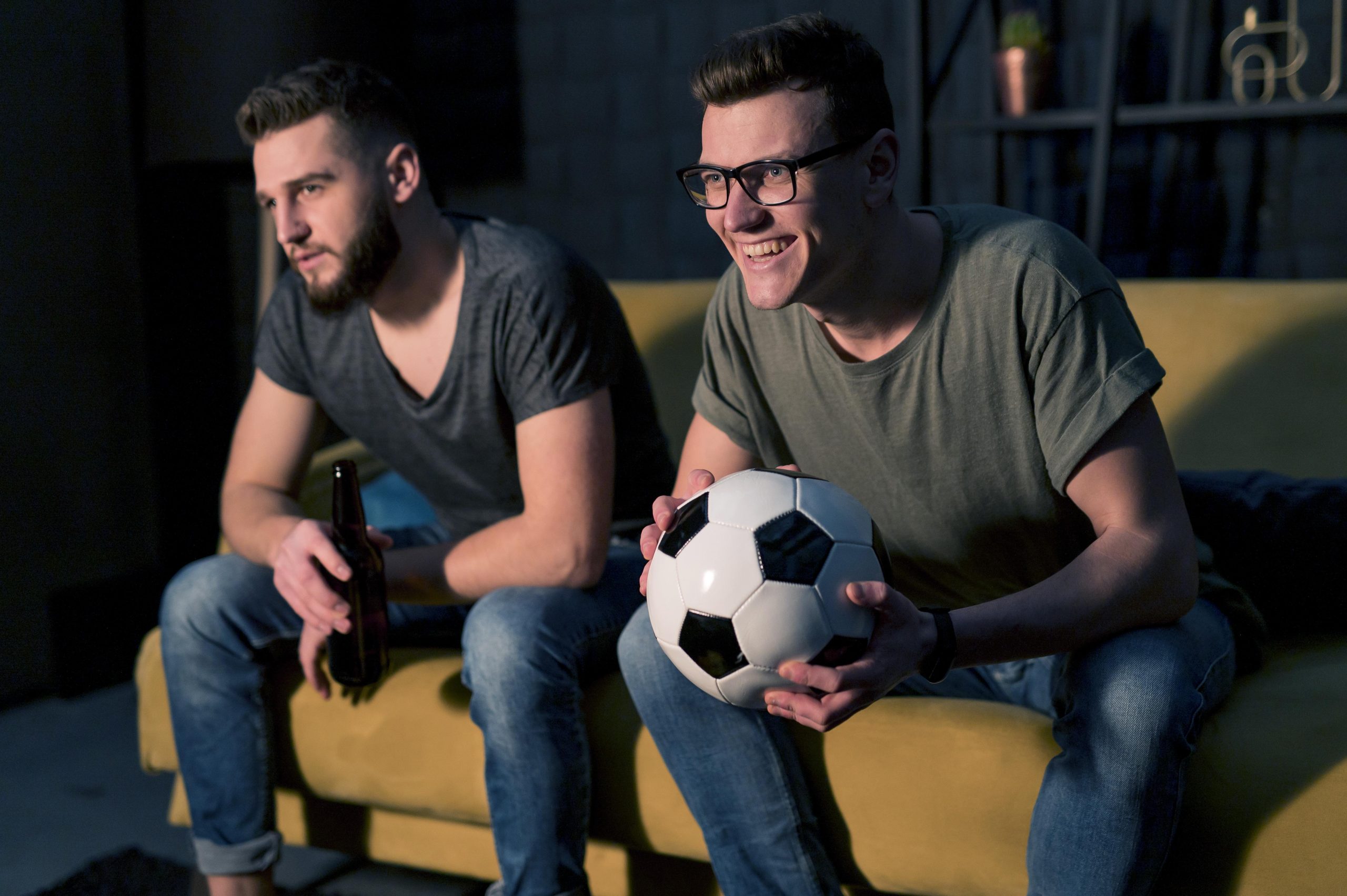 smiley male friends watching sports tv together while holding football scaled